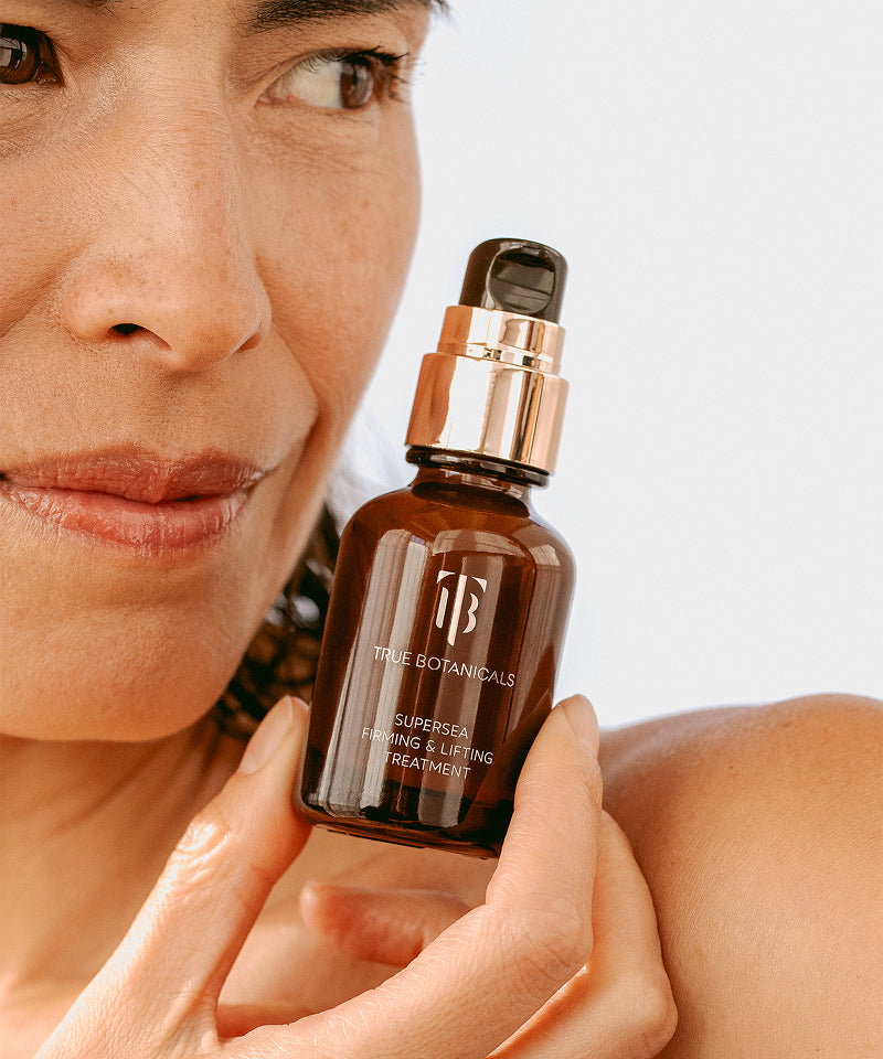 Woman holding a bottle of True Botanicals SuperSEA Firming & Lifting Treatment, showcasing the product's packaging and texture.