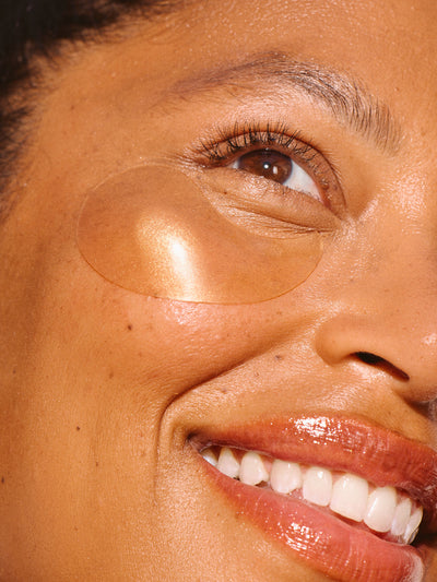 Model close up wearing eye patches with glowing skin.