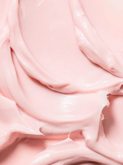 Close-up texture shot of True Botanicals Chebula Extreme Cream showing a thick, luxurious blush-pink cream with a glossy, whipped consistency and soft swirled folds.