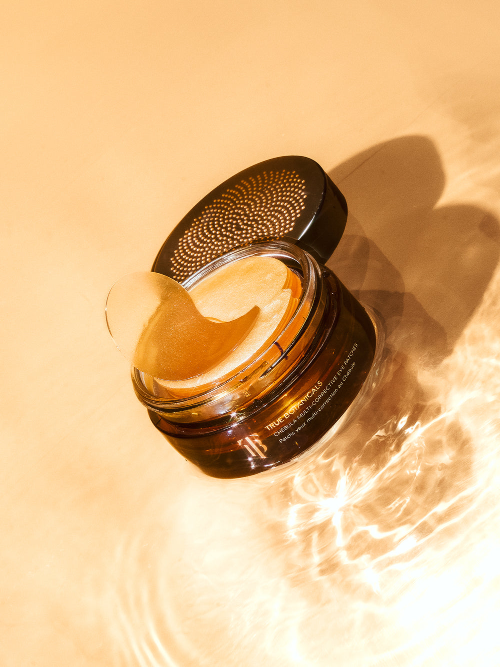 This image shows a luxurious jar of eye masks or treatment patches with shimmering golden tones. The sleek black lid with an intricate dotted design adds elegance and modernity. Ideal for highlighting skincare focused on brightening, hydrating, and rejuvenating the under-eye area.