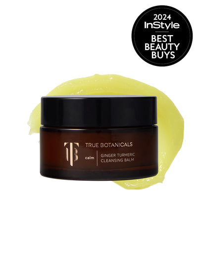 A jar of True Botanicals Ginger Turmeric Cleansing Balm in a dark amber container with a black lid is displayed against a white background. Behind the jar, a smooth, golden-yellow balm is swirled. A black circular badge in the top right corner reads "2024 InStyle Best Beauty Buys."