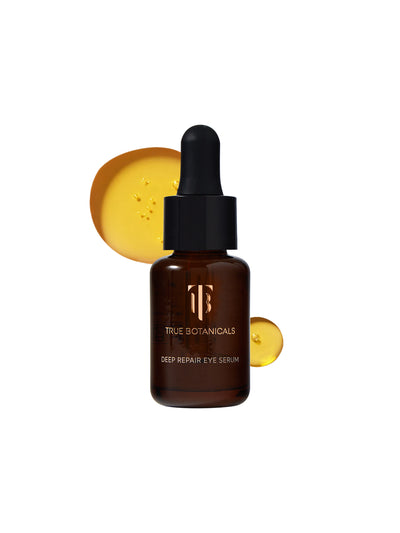 A clean product image of True Botanicals Deep Repair Eye Serum. The amber glass bottle with a black dropper cap is displayed prominently against a white background. Behind it, golden drops of the serum are shown, highlighting the product's rich and nourishing texture.