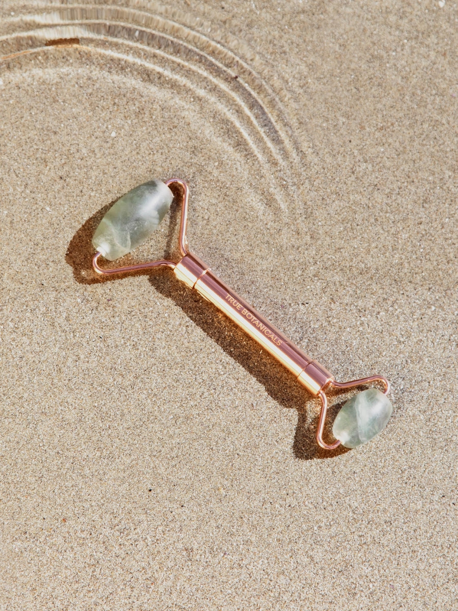 Rose gold facial roller with jade stones on a sandy background