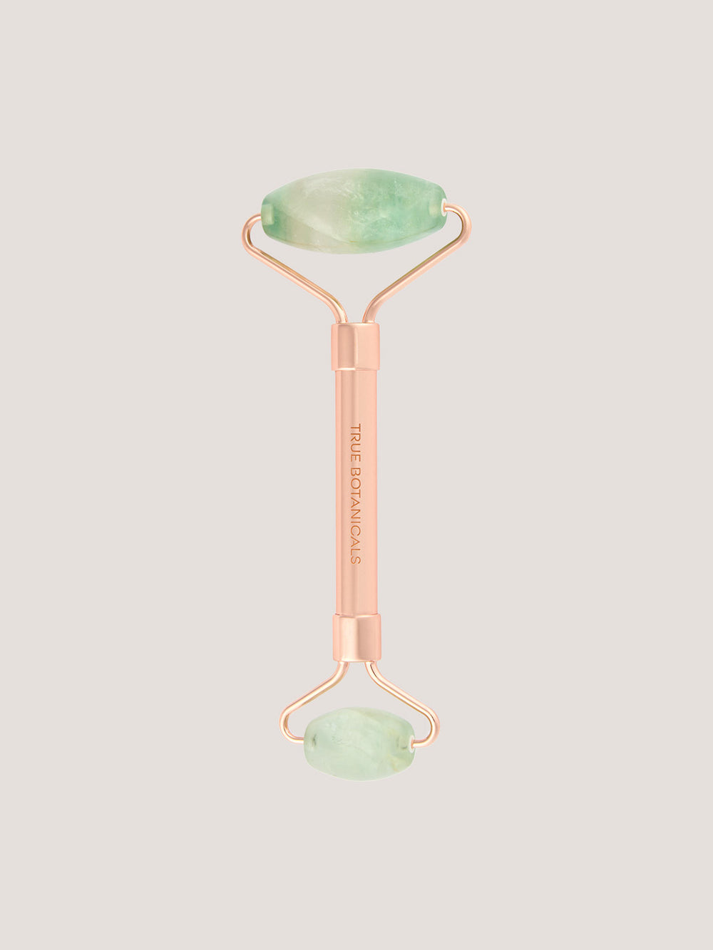 Rose gold facial roller with green jade stones on a light gray background