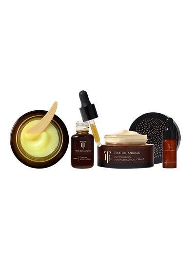 A clean, minimalist display of True Botanicals skincare products. Featured items include the Ginger Turmeric Cleansing Balm with a wooden applicator, Chebula Active Serum with a dropper, Phyto-Retinol Advanced Clinical Cream with its luxurious texture, and Renew Pure Radiance Oil, all in sleek amber and black packaging. Perfectly arranged against a white background for a sophisticated look.