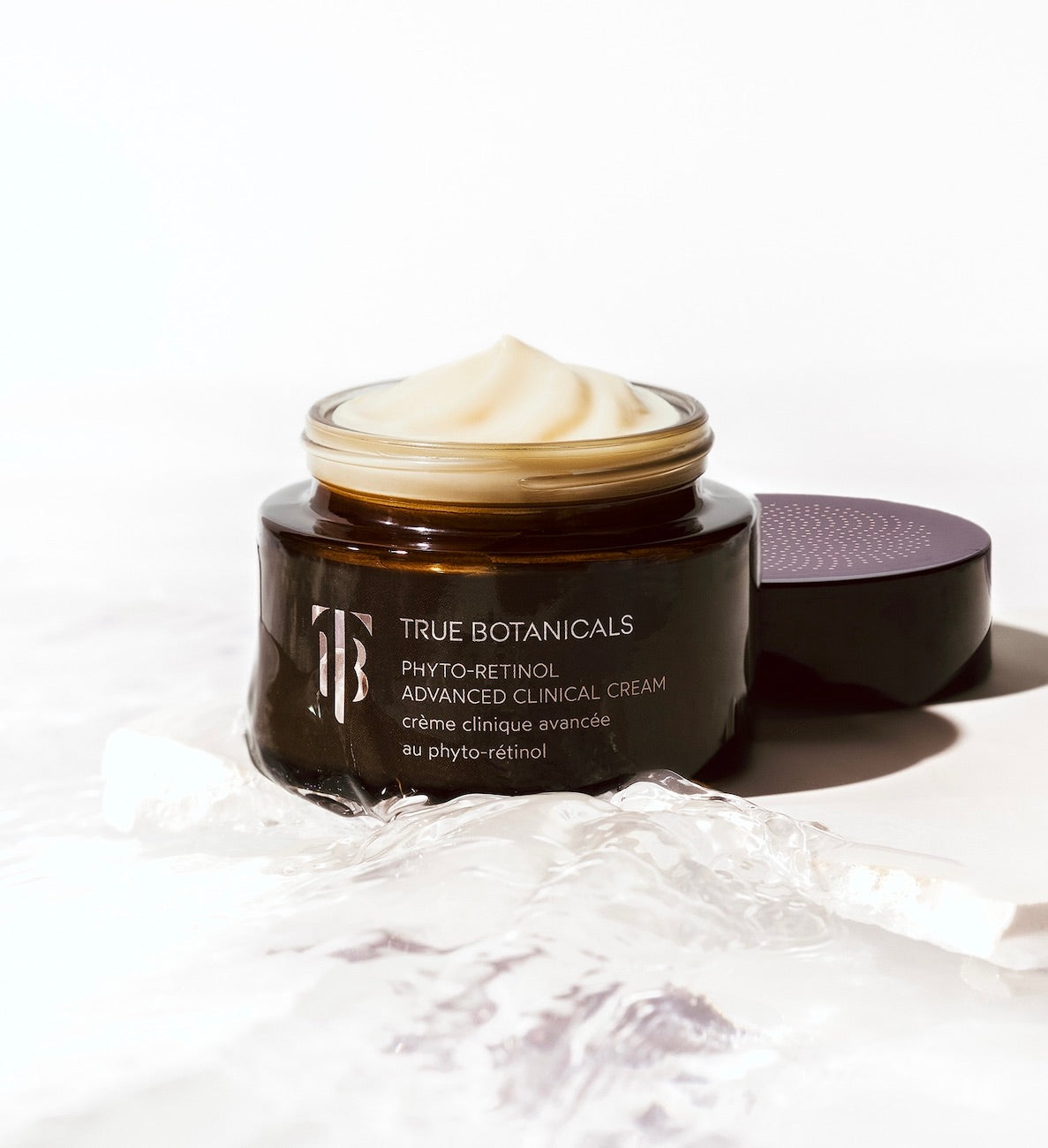 True Botanicals Phyto-Retinol Advanced Clinical Cream in an amber glass jar with a smooth, whipped texture, set against a clean background with water elements, highlighting hydration and luxury.