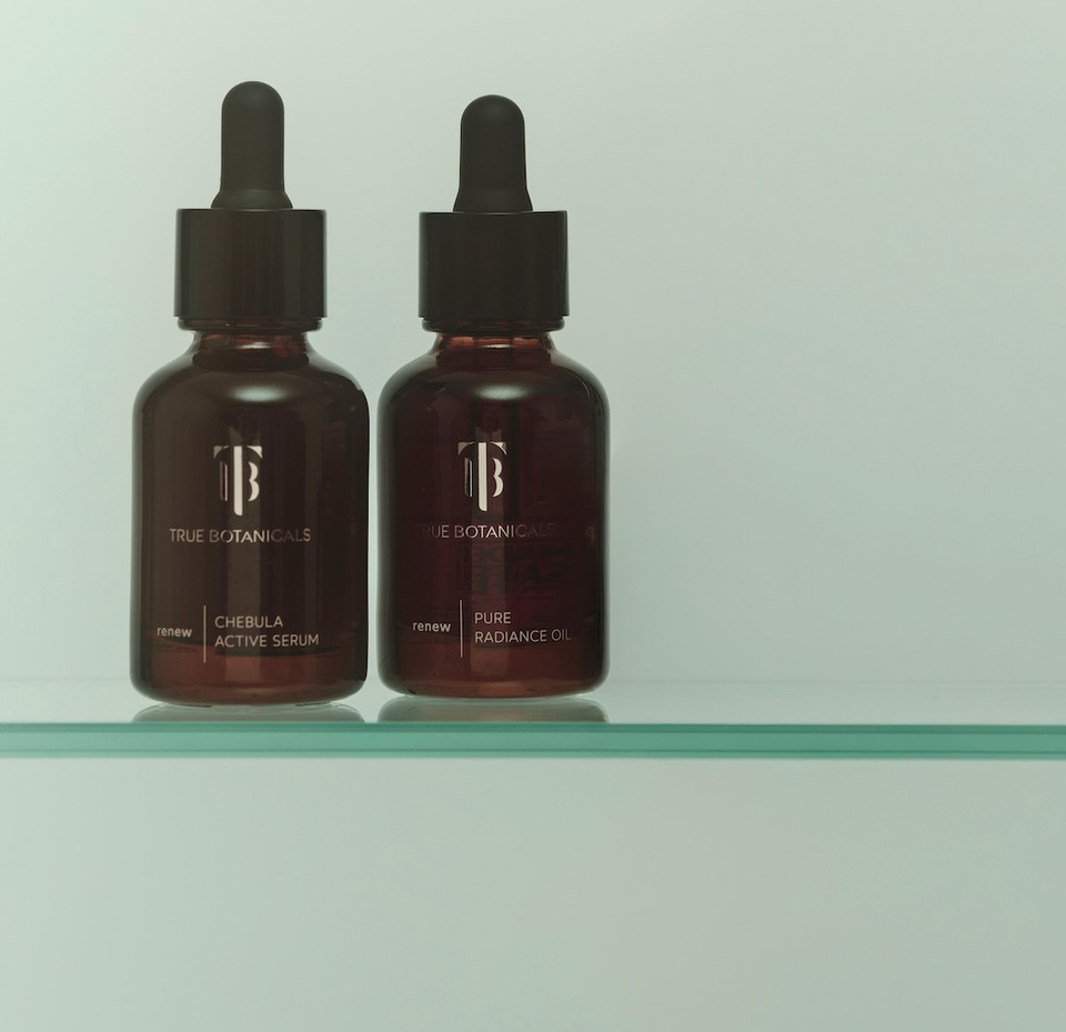 Two bottles of True Botanicals serum on a glass shelf with a light gray background