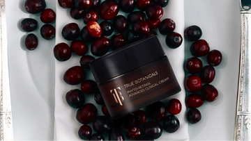 Jar of cream surrounded by berries on a white plate with cutlery against a red background