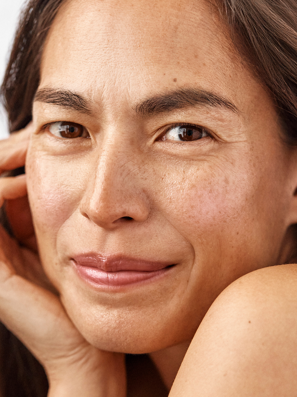 Close-up of a woman's face with a soft smile and hand on her cheek.
