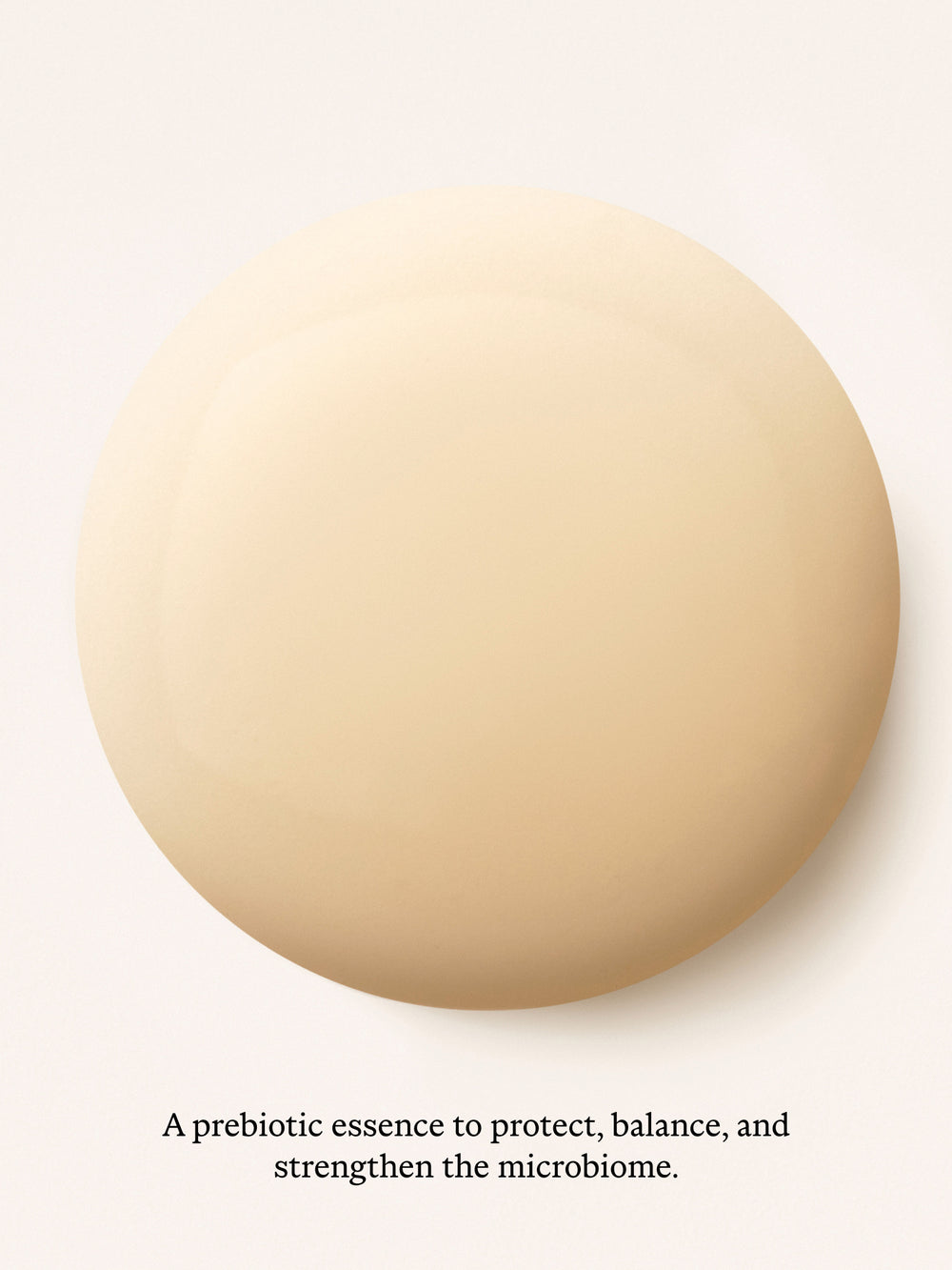 A large smooth beige circular swatch centered on a white background, with small black text below reading, 'A prebiotic essence to protect, balance, and strengthen the microbiome.'.