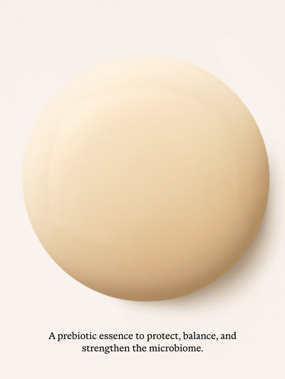 A large smooth beige circular swatch centered on a white background, with small black text below reading, 'A prebiotic essence to protect, balance, and strengthen the microbiome.'.