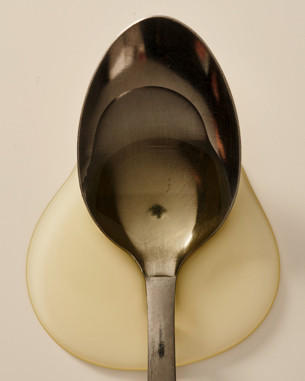 Close-up of a metal spoon resting over a glossy pool of Mindful Mama Belly & Body Oil.