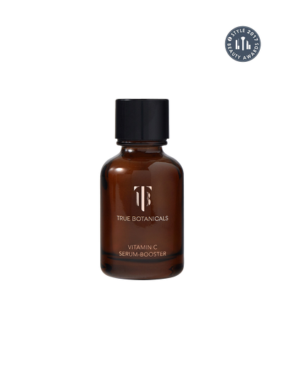 A brown amber glass bottle of True Botanicals Vitamin C Serum-Booster with a black cap, shown on a plain white background with a circular award badge in the top right corner.