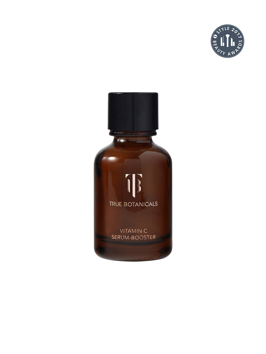 A brown amber glass bottle of True Botanicals Vitamin C Serum-Booster with a black cap, shown on a plain white background with a circular award badge in the top right corner.